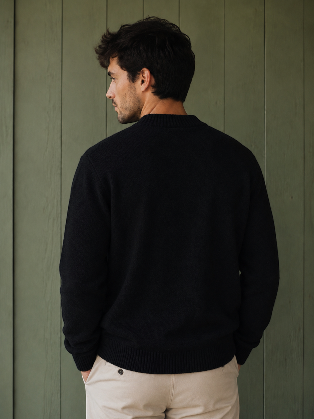 Man wearing a black KZ DIFFUSION wool blend sweater, back view, against a green wooden wall.