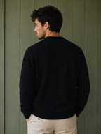 Man wearing a black KZ DIFFUSION wool blend sweater, back view, against a green wooden wall.