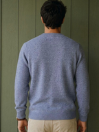 Back view of a man wearing a blue KZ DIFFUSION wool blend sweater with ribbed cuffs against a green wooden wall