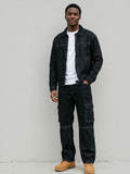 A man wearing a BROCK black denim jacket and matching cargo pants with white t-shirt and tan boots.