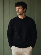 Man wearing a black KZ DIFFUSION wool blend sweater with a crew neck, standing against a green wooden wall.