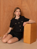 Femme portant le top manches courtes noir FRIME de BROCK avec boutons dorés, style chic et décontracté