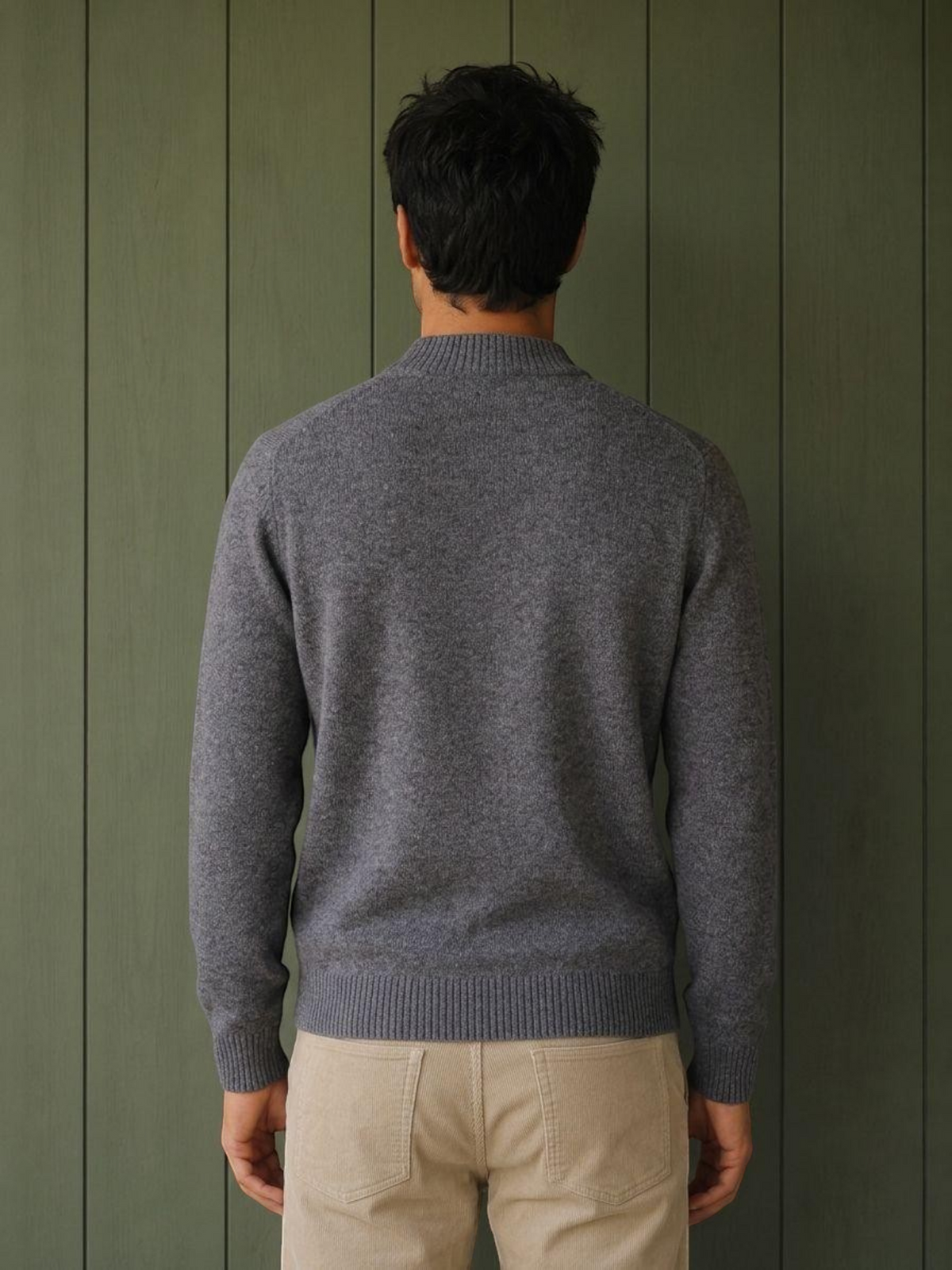 Back view of a man wearing a grey KZ DIFFUSION wool blend sweater with a ribbed collar and cuffs against a green wall