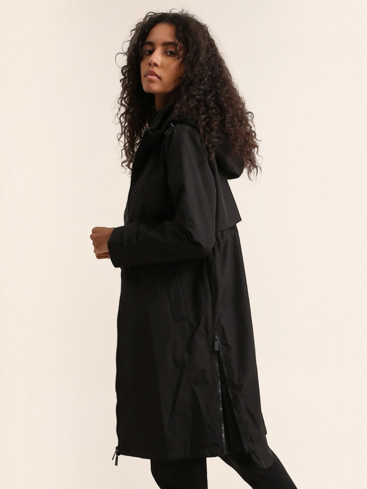 Model wearing a black BROCK ATTRAIT PARIS long waterproof hooded jacket with side zip details