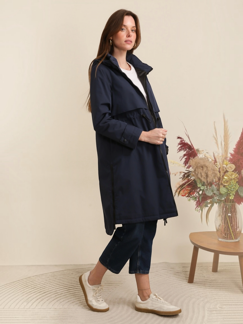 Model wearing a navy blue BROCK ATTRAIT PARIS long waterproof hooded jacket with an adjustable waist and light lining.