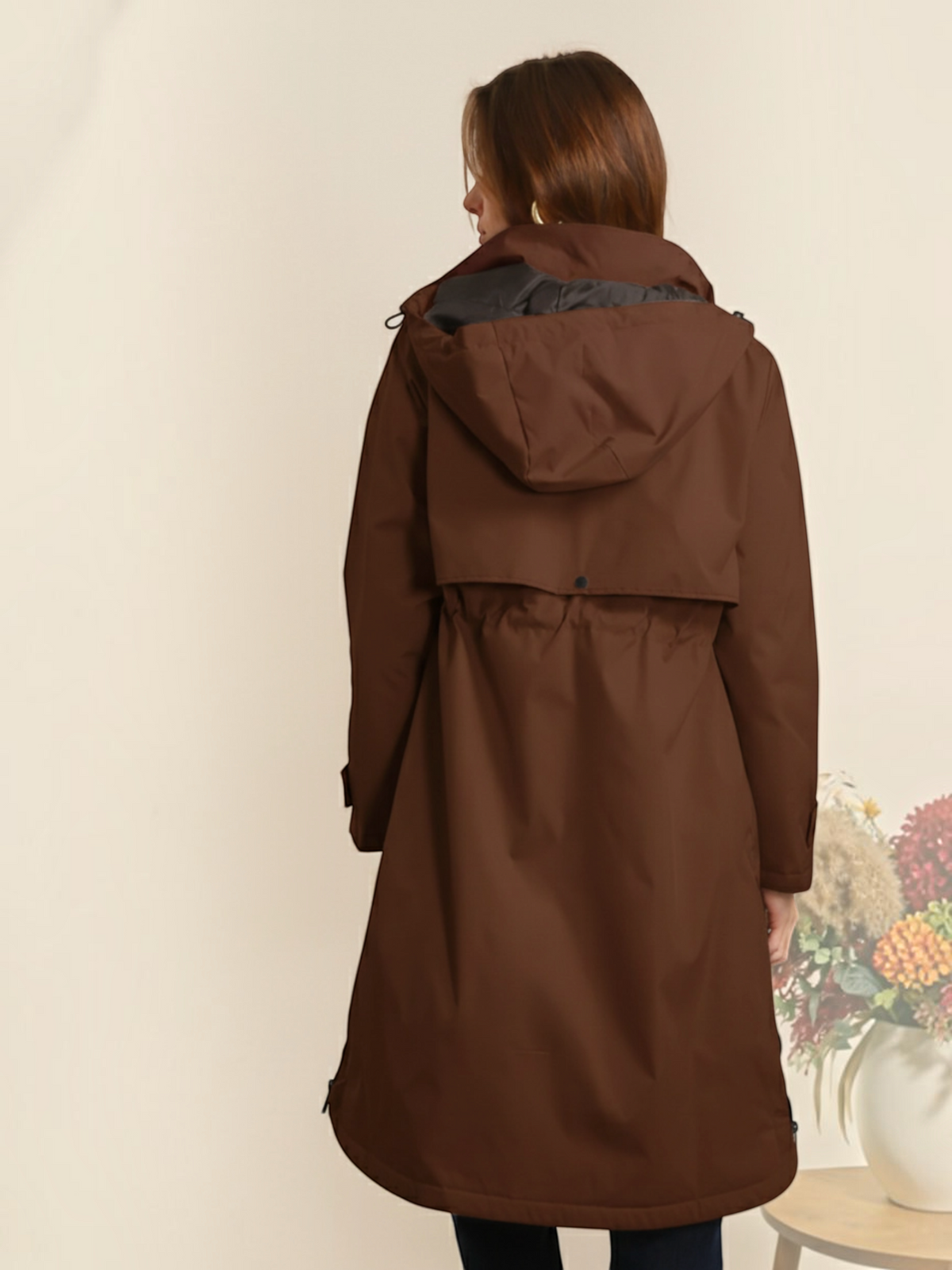 Woman wearing a brown BROCK long waterproof hooded jacket with an adjustable waist, back view.