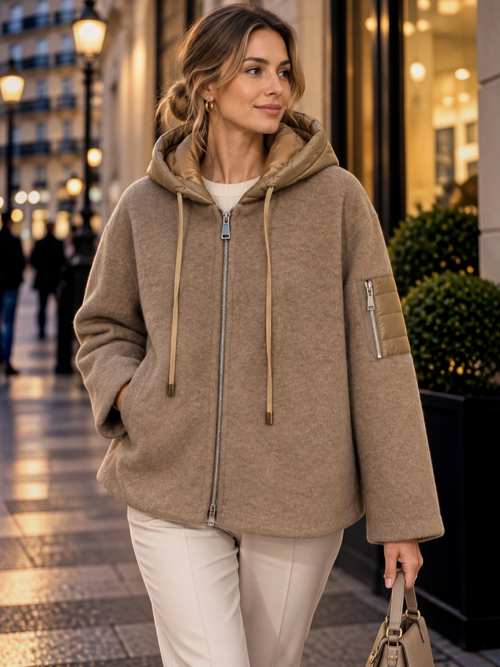 Woman wearing a BROCK beige felted wool-blend zip-up jacket with a quilted hood and sleeve pocket on a city street.