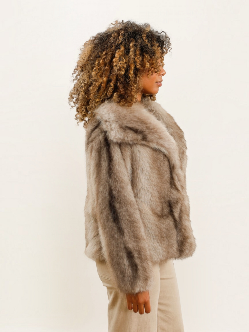 Modèle portant un manteau oversize BROCK DIX-ONZE en fausse fourrure beige avec un large col structuré, vue de profil.
