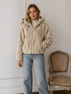 Veste courte zippée en fausse fourrure beige BROCK avec capuche à cordons portée par une femme