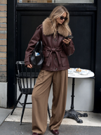 Manteau mi-long en similicuir marron BROCK avec col en fausse fourrure, ceinture à nouer et poches plaquées.