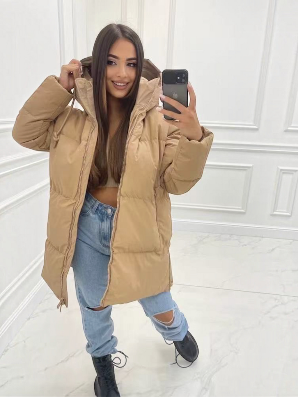 Doudoune mi-longue matelassée beige BROCK avec capuche, portée par une femme avec un jean bleu et des bottines noires.