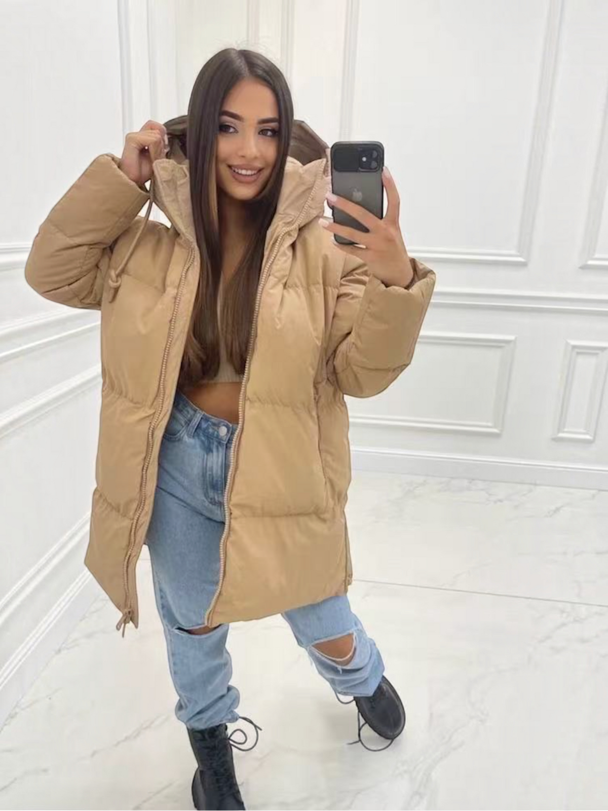 Doudoune mi-longue matelassée beige BROCK avec capuche, portée par une femme avec un jean bleu et des bottines noires.