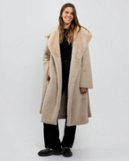 Femme portant un manteau long beige en fausse fourrure BROCK avec grand col à revers et ceinture à nouer