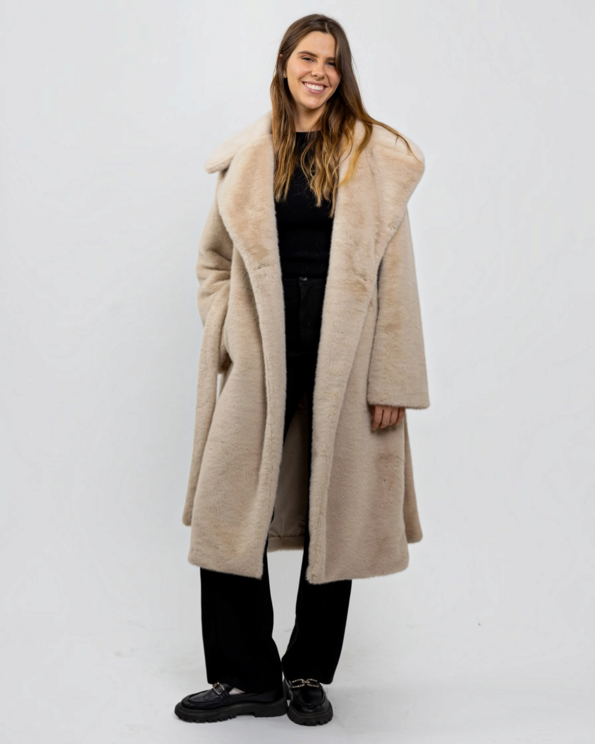 Femme portant un manteau long beige en fausse fourrure BROCK avec grand col à revers et ceinture à nouer