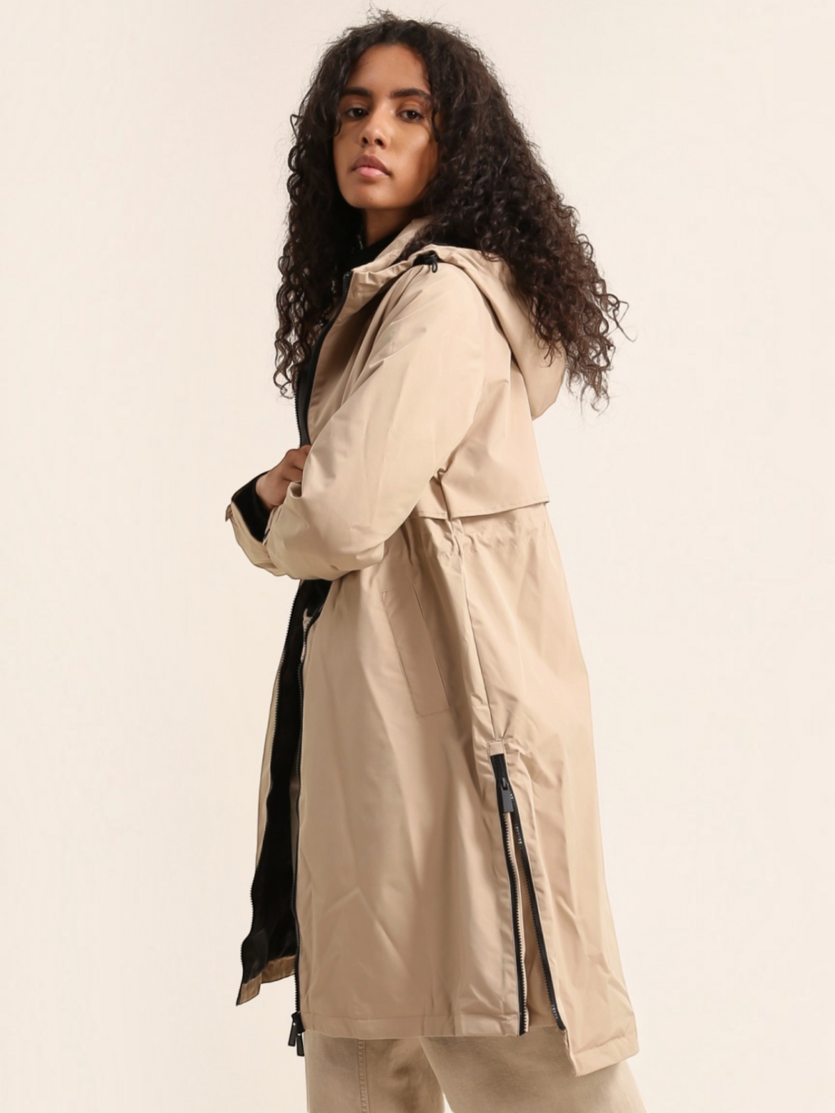 Model wearing a beige BROCK ATTRAIT PARIS long waterproof hooded jacket with black lining and side zippers