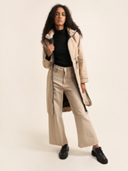 Model wearing a beige BROCK ATTRAIT PARIS long waterproof hooded jacket with a black lining and adjustable fit.