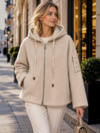 Woman wearing a beige BROCK felted wool-blend zip-up jacket with a quilted hood and sleeve pocket on a city street.