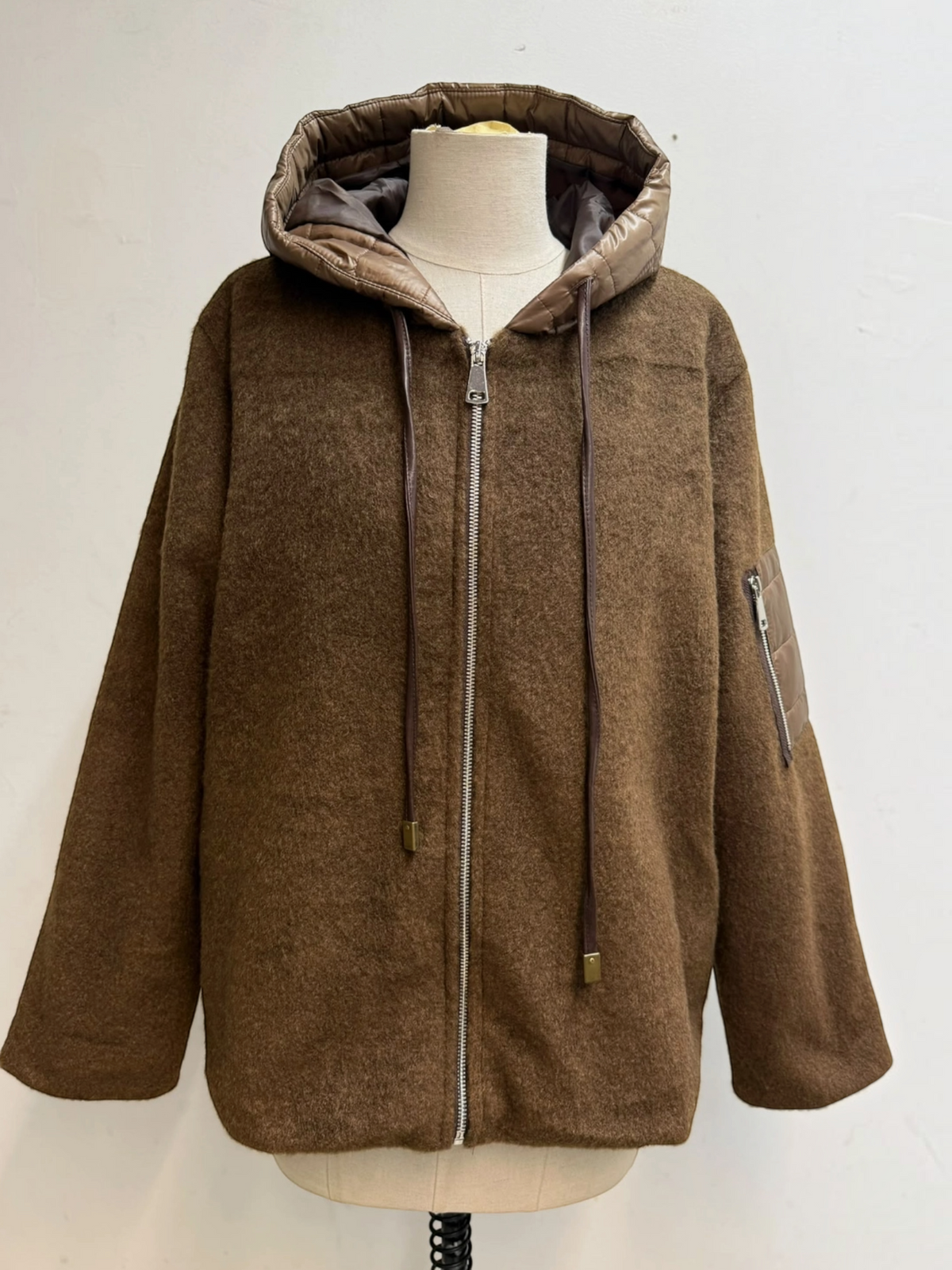 BROCK brown felted wool-blend zip-up jacket with a quilted hood, drawstring ties, and a sleeve pocket on a mannequin.