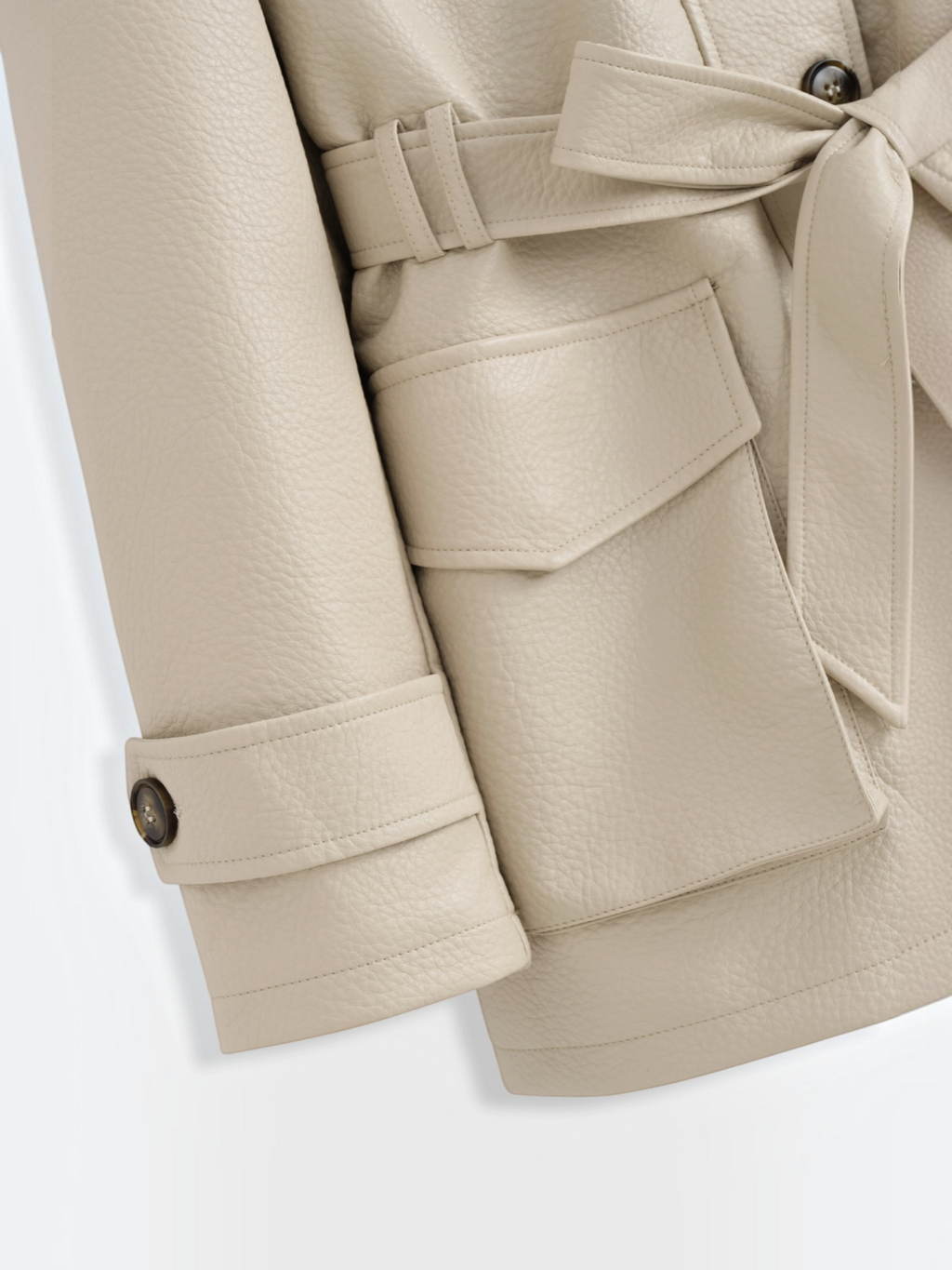 Détail du manteau mi-long BROCK en similicuir beige avec ceinture à nouer, poches à rabat et boutons contrastants