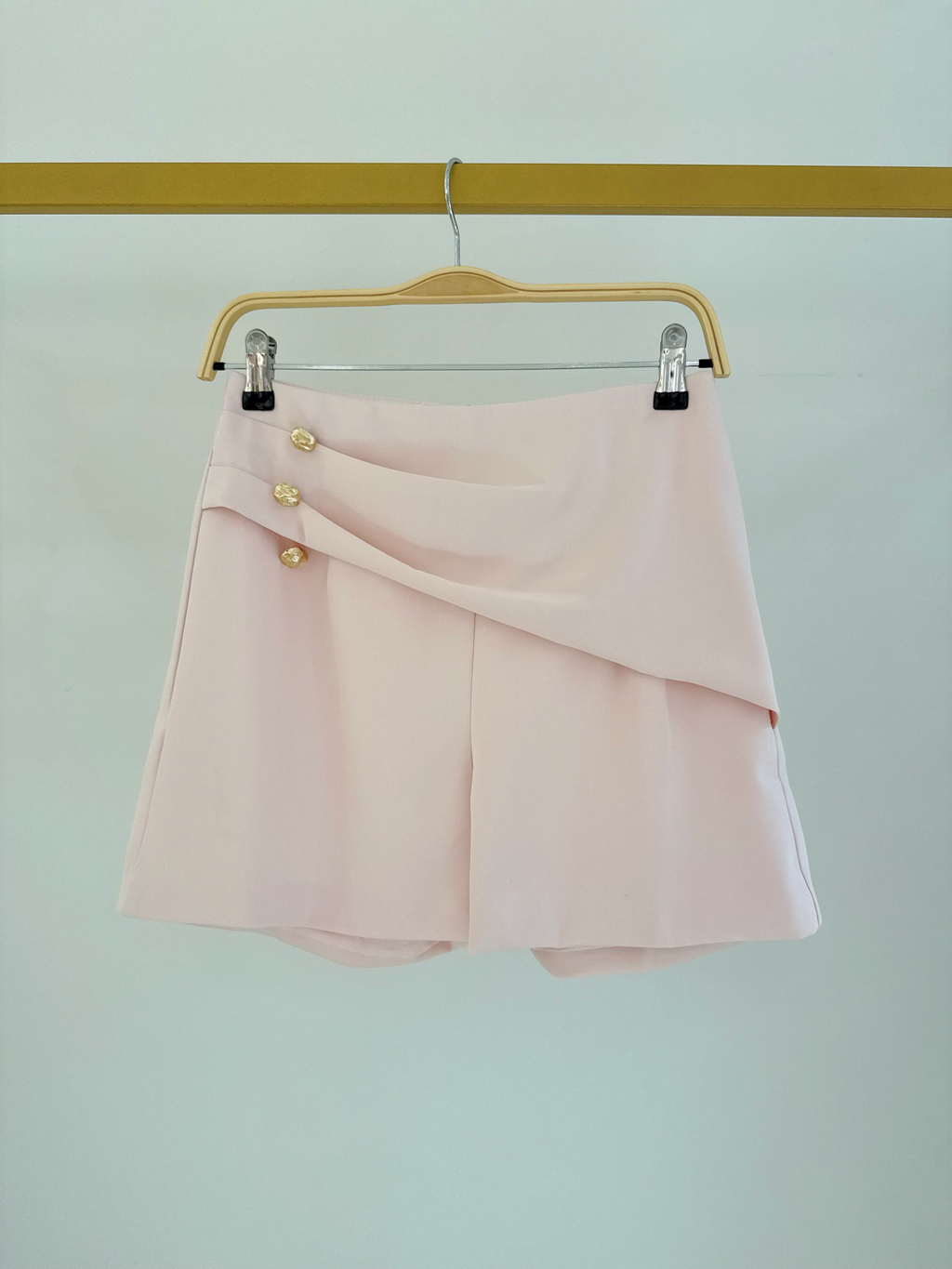 Short taille haute rose BROCK avec boutons dorés décoratifs, en polyester, suspendu sur un cintre.
