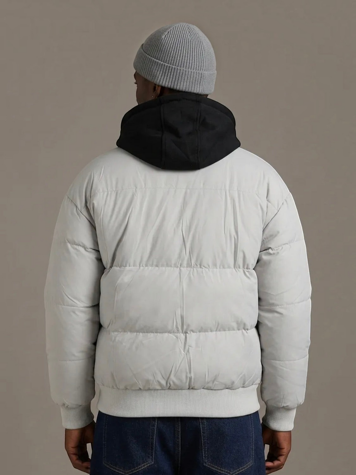 Back view of a man wearing a grey BROCK puffer jacket with a detachable black hood and ribbed hem