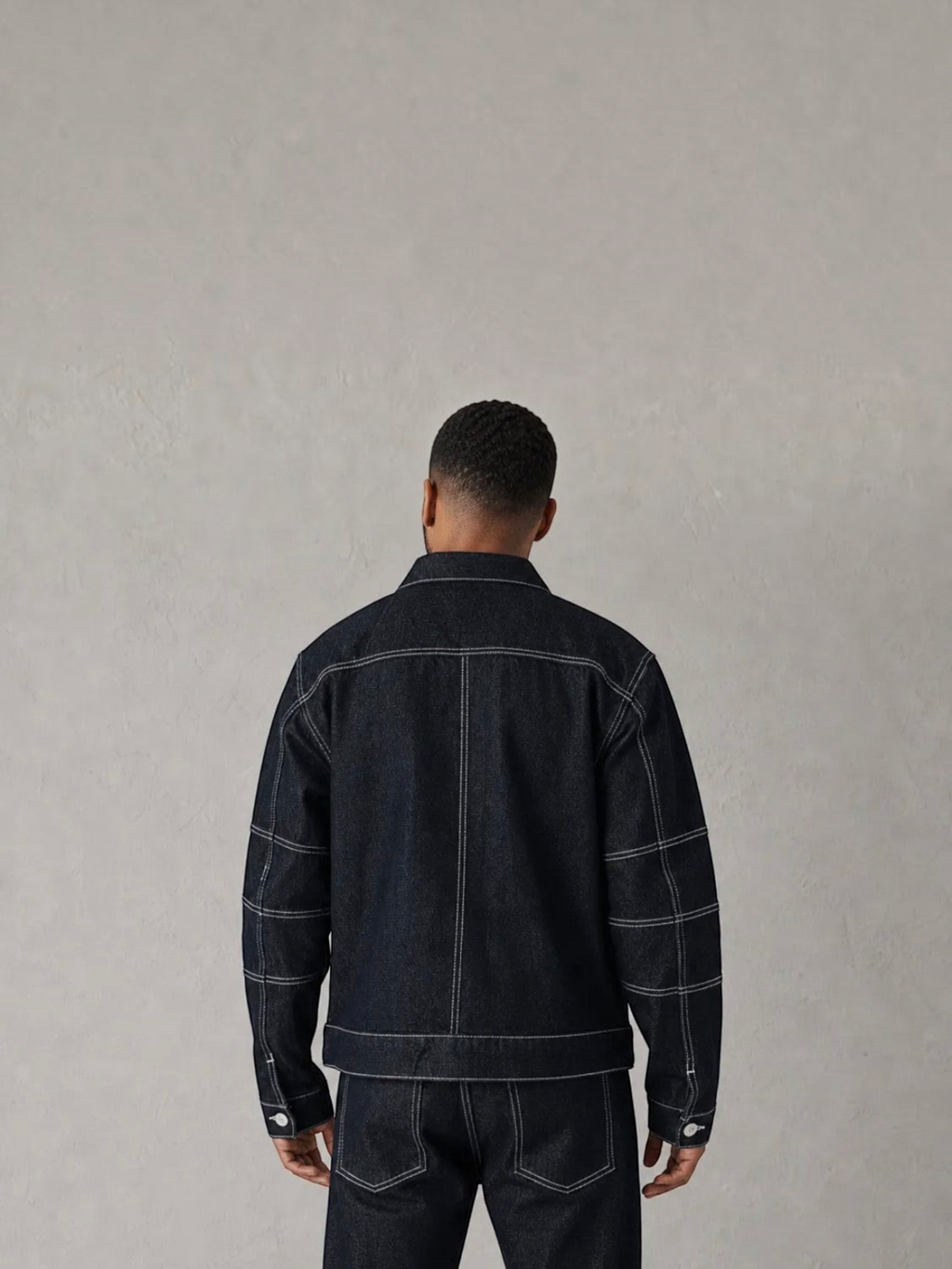 Back view of a man wearing a BROCK dark blue denim jacket and matching jeans with white contrast stitching.