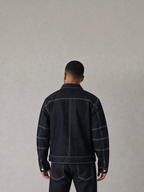 Back view of a man wearing a BROCK dark blue denim jacket and matching jeans with white contrast stitching.