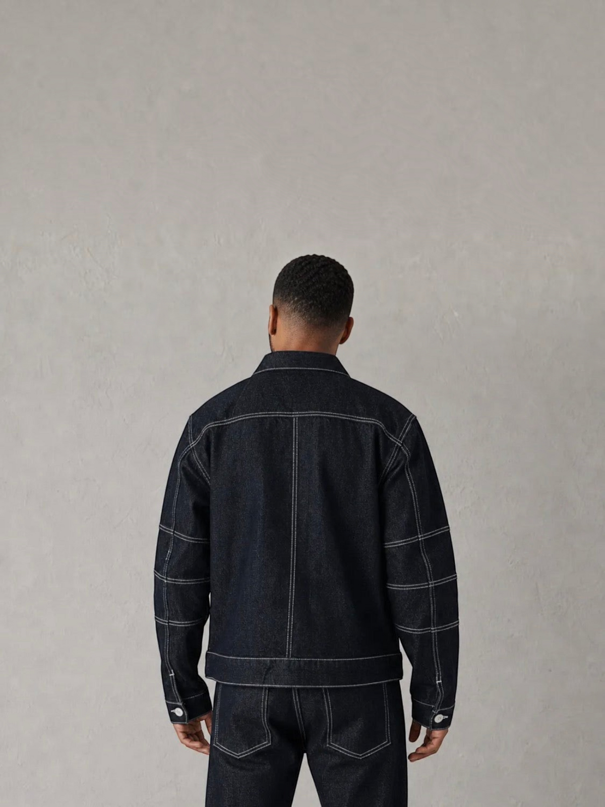 Back view of a man wearing a BROCK dark blue denim jacket and matching jeans with white contrast stitching.
