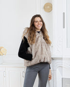 Woman wearing a BROCK beige two-tone faux fur hooded vest over a black sweater in a bright interior