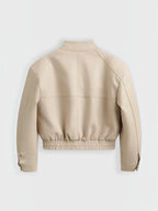 Back view of a beige BROCK faux leather cropped jacket with a stand collar and elasticated hem.
