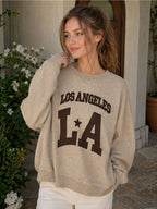 BROCK beige cotton knit sweater with Los Angeles LA graphic print worn by a woman in a casual outdoor setting