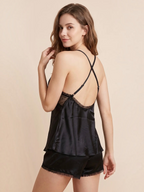 Model wearing a black BROCK BELLE COM'ELLE satin pajama set with lace trim and adjustable crisscross back straps.