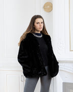 Woman wearing a black BROCK faux fur hooded coat with a velvet-touch finish in a classic interior setting.