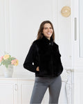Woman wearing a black BROCK faux fur sleeveless vest with a front zipper and side pockets in a bright room.