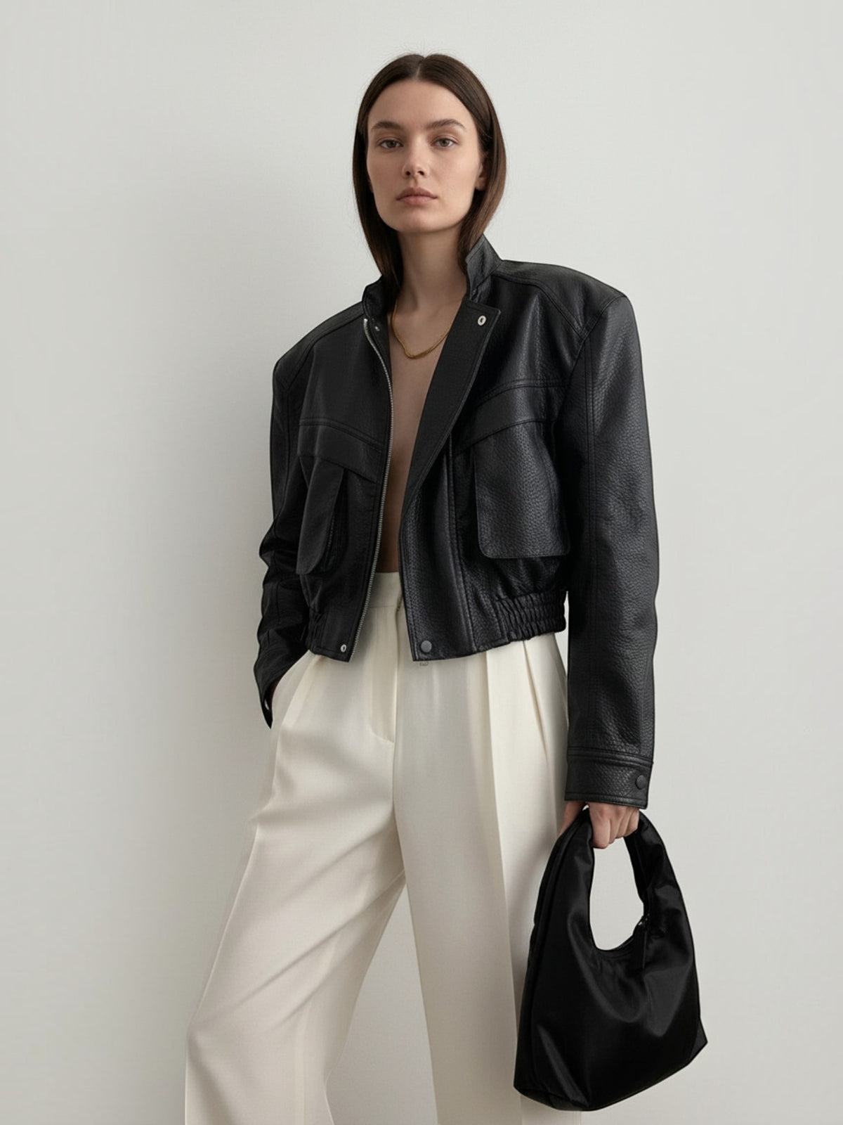 Model wearing a BROCK black faux leather cropped jacket with structured shoulders, flap pockets, and elastic hem.