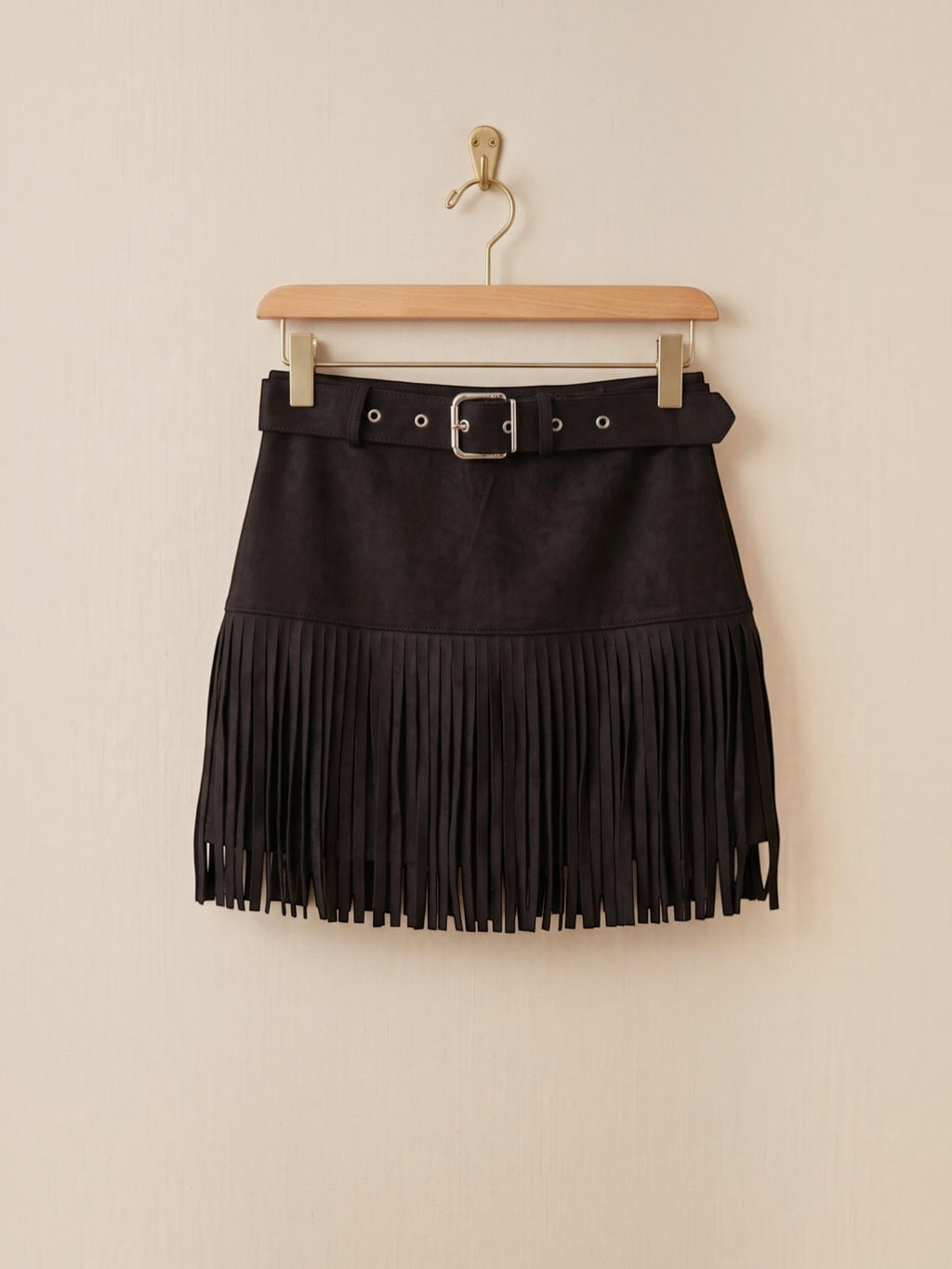 BROCK black faux suede mini skirt with fringe hem and matching belt featuring a silver buckle hanging on a hanger