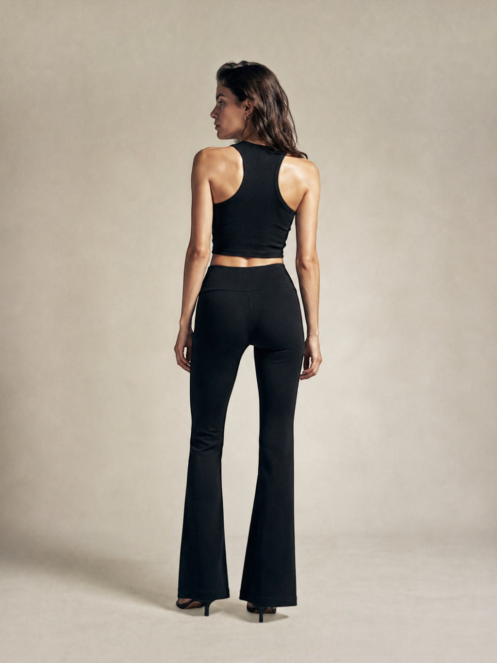 Model wearing BROCK black high-waisted flared leggings and a matching racerback crop top, back view.