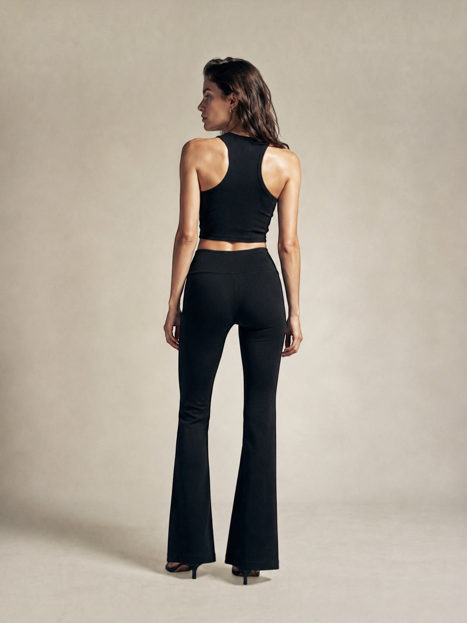 Model wearing BROCK black high-waisted flared leggings and a matching racerback crop top, back view.