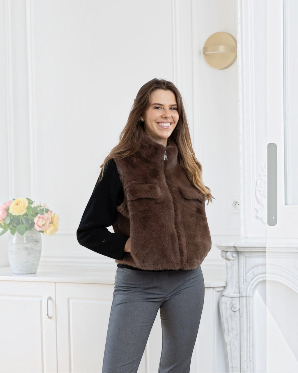 Woman wearing a brown BROCK faux fur sleeveless vest with a front zipper and pockets over a black sweater