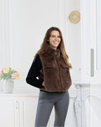 Woman wearing a brown BROCK faux fur sleeveless vest with a front zipper and pockets over a black sweater