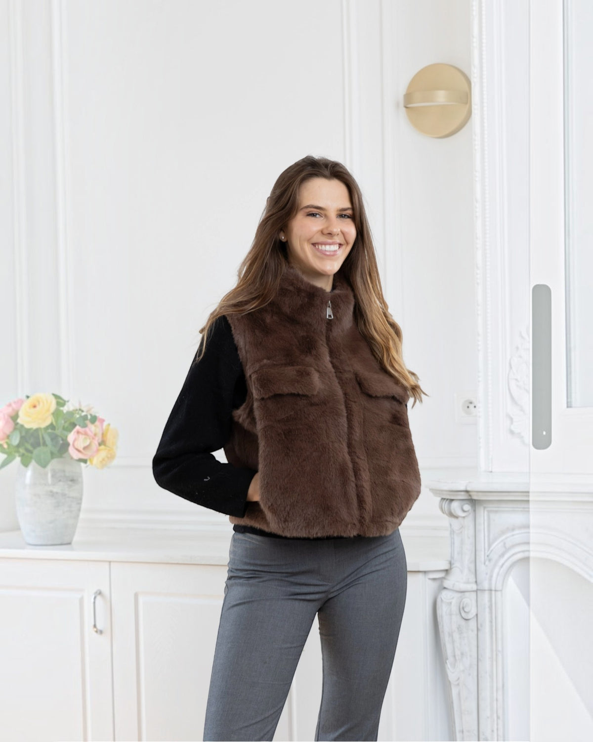 Woman wearing a brown BROCK faux fur sleeveless vest with a front zipper and pockets over a black sweater