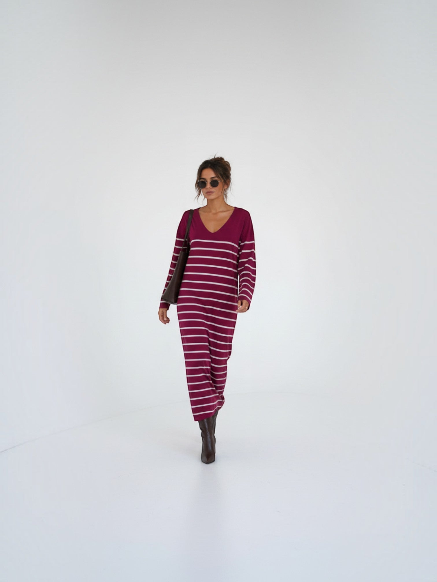 BROCK model wearing a long burgundy striped maxi dress with a V-neck and long sleeves in a minimalist studio setting.