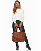 A woman holding a large cognac brown BROCK faux leather tote bag with decorative tassel zippers and shoulder strap.