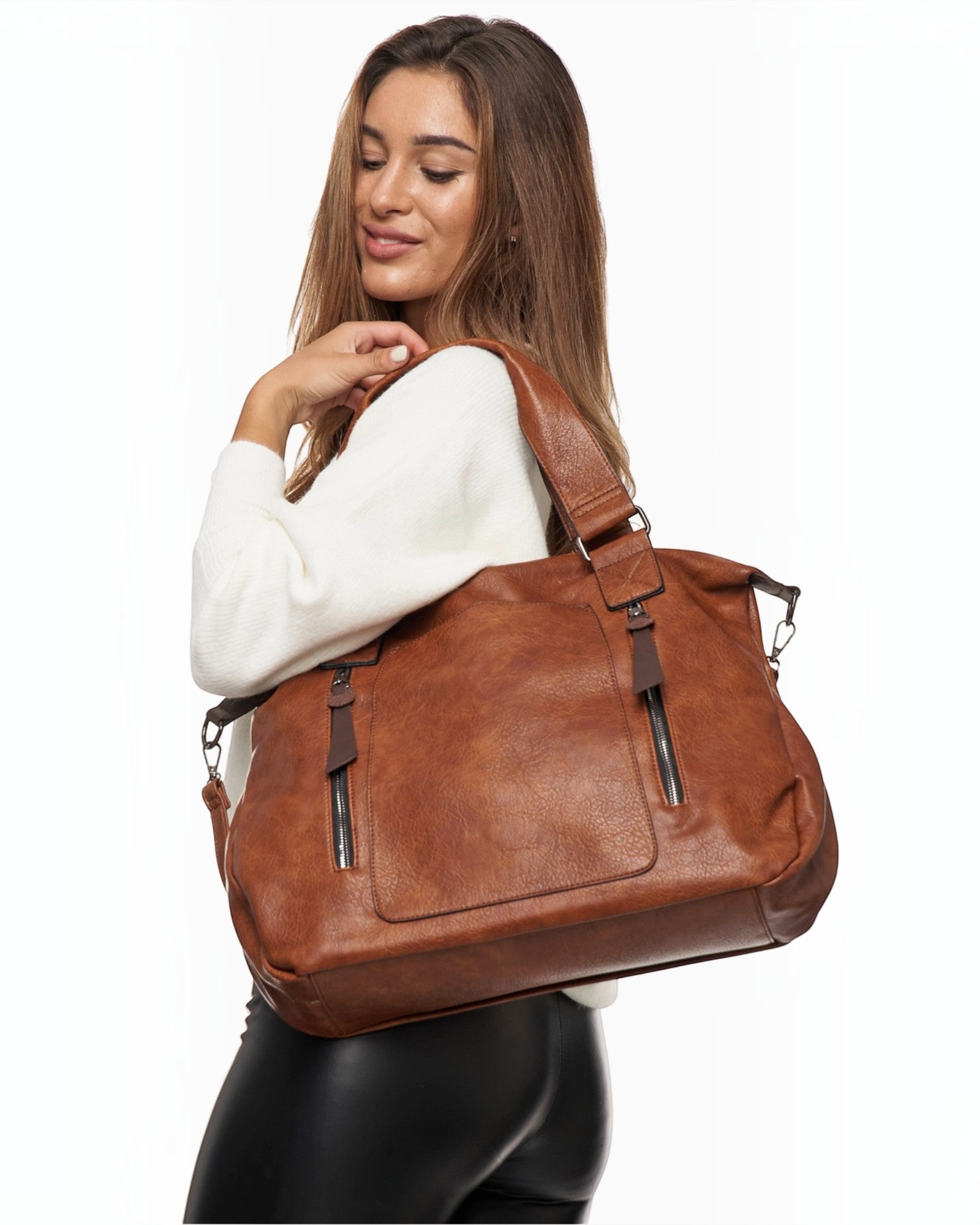 A woman wearing a large cognac-colored BROCK faux leather tote bag with decorative zipper tassels over her shoulder.