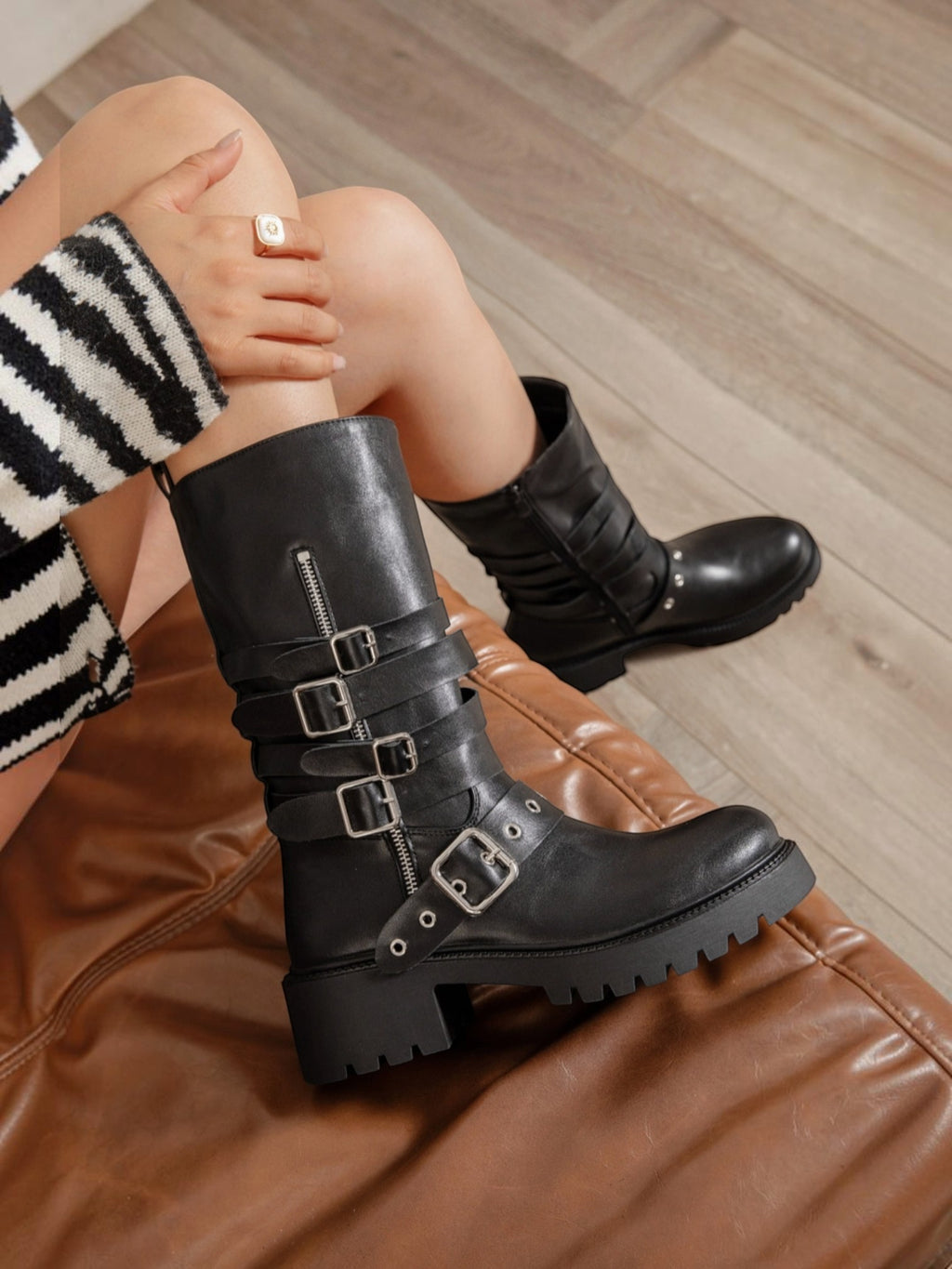 BROCK ERYNN black rock-style boots with multiple buckle straps, side zip, and thick lug soles on a leather chair.