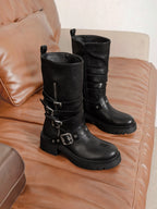 BROCK ERYNN black rock-style boots with metallic buckles, adjustable straps, and thick lug soles on a leather sofa.