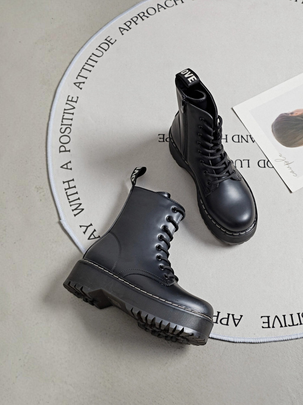 BROCK ERYNN black combat boots with platform lug soles, lace-up front, side zipper, and white contrast stitching.