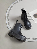 BROCK ERYNN black combat boots with platform lug soles, lace-up front, side zipper, and white contrast stitching.