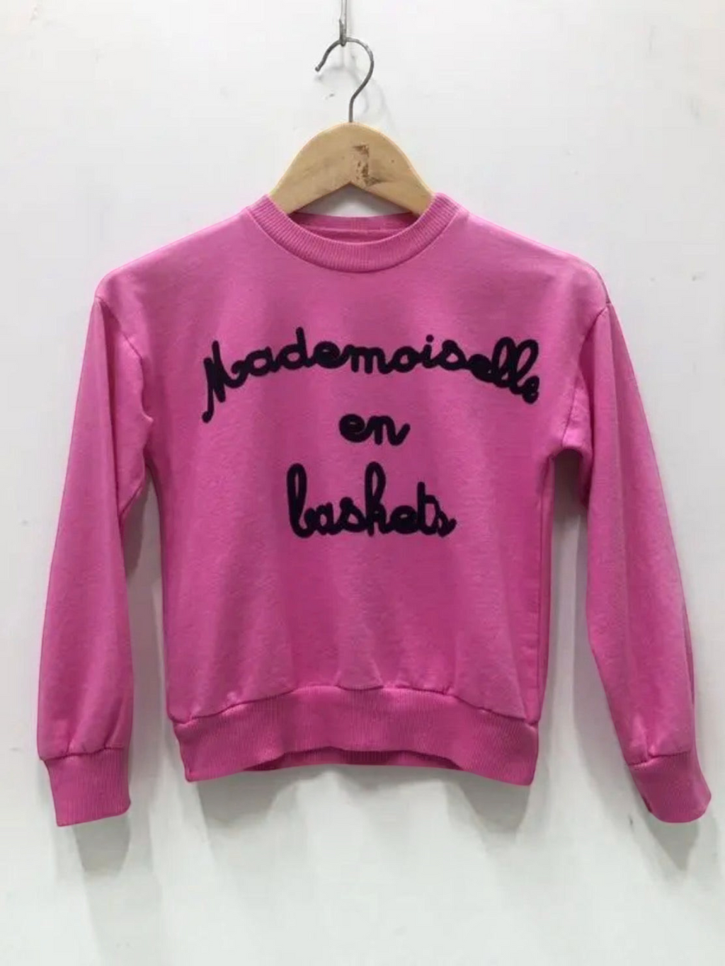 BROCK fuchsia cotton sweatshirt for children with Mademoiselle en baskets text embroidery on a wooden hanger