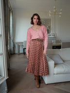 Model wearing a BROCK pleated midi skirt with geometric print, styled with a pink cardigan and brown belt